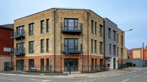 Slough Borough Council A three-story block of flats with a modern-looking brick exterior with black window frames and balconies.