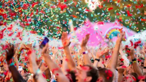 A picture of the crowd cheering as rainbow confetti falls.