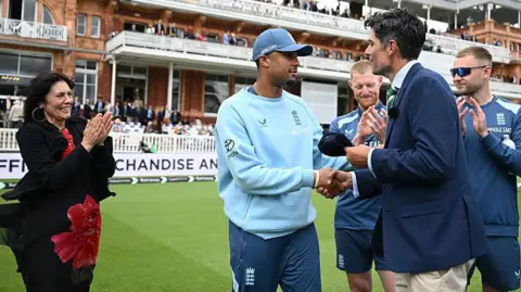 Getty Images Durham opening batsman Emilio Gay receives his England test cap from Sir Alastair Cook ahead of the Test Match between England and New Zealand at Lord's Cricket Ground on June 04, 2026 in London, England. They are shaking hands, and all wearing blue. 