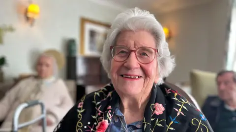 George Carden/BBC Wendy spragg who has grey hair and glasses wearing a floral shawl draped over her shoulders