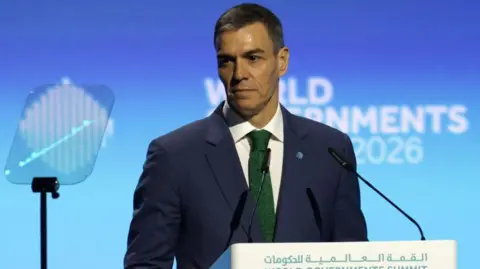 EPA/Shutterstock Pedro Sanchez, wearing a blue blazer and dark green tie, standing at the lectern at the World Government's summit. It's a bright blue background.