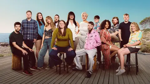 Channel 4 A promotional image of 14 people who are either sitting on stools or standing. They are on an island next to a beach.