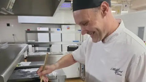 Supplied A chef smiling as he stirs a pot