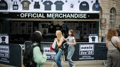 A girl and a woman walk past a stand selling Oasis merchandise set up in Manchester. 