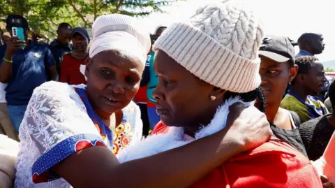 Two women, one in a white headscarf and the other in a beanie hat embracing