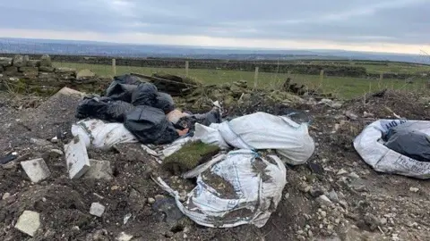 Gemma Dillon/BBC Large bags of rubbish and building waste dumped near a field.