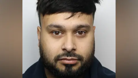 A police mugshot of a man with black hair and beard