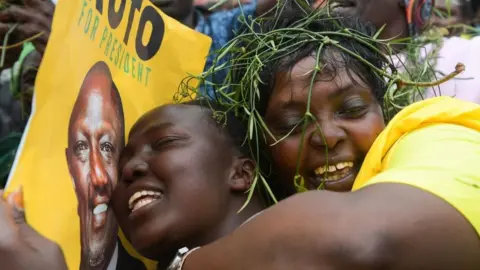 Residents hold posters of Kenya's Deputy President and presidential candidate of Kenya Kwanza (Kenya First) political party coalition William Ruto while they watch a live broadcast as they wait for the results of Kenya's national election in Eldoret on August 15, 2022