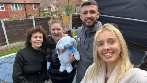 Wendy Hughes An older woman, two young women and a young man stand smiling at the camera as the young woman on the right takes a "selfie". The other young woman is holding a blue stuffed rabbit.