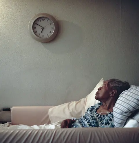 Nicola Muirhead An elderly lady lying in bed looking at a wall clock