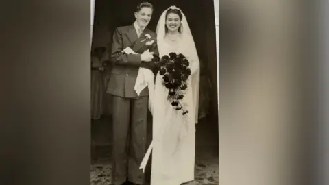 Supplied Bill and Olive Miles pictured at Guildford Cathedral on 15th November 1952, their wedding day. Bill is wearing a suit with a flower, while Olive is wearing a long white dress and veil. She is also holding flowers. 