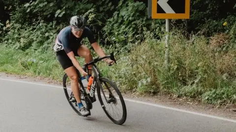 Angela Mills-Bannon Angela Mills-Bannon on a bike pedalling around a corner on a road.