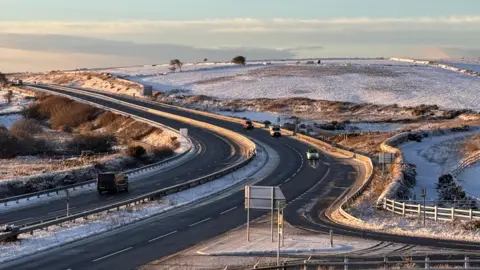 Jonathan Fielding The A30 at Temple, Bodmin is surrounded by snowy fields. There are very few cars on the road and there is a pale blue sky.