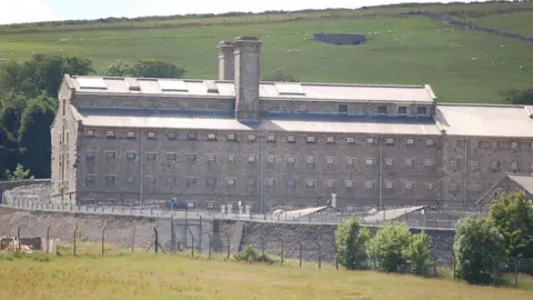 A large prison can be seen from afar, surrounded by rolling hills and fields