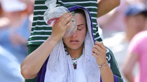 Getty Images Tennis player Aryna Sabalenka holds ice on her head and covers herself with a towel during the Ladies' Singles semi-final at Wimbledon on 10 July 2025 in London, England.