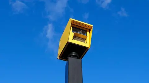 A yellow speed camera against a blue sky