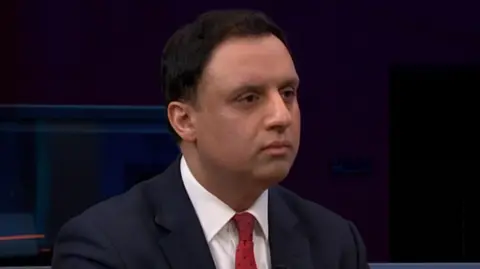 Anas Sarwar in a dark suit with a white shirt and purple tie