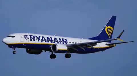 A Ryanair plane descends in a clear blue sky over Liverpool.