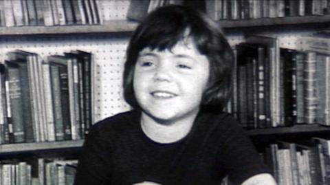 A child smiling in front of bookshelves during the interview