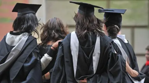 The back of four women's heads. Three of them wear graduation caps and gowns