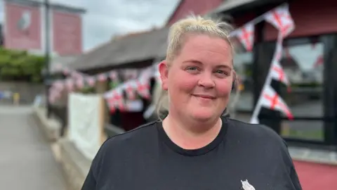 Dawn Payne in a black T-shirt standing outside the Old Barn Inn with England flag bunting in the background