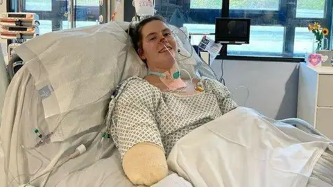 Tanya Gorrod and Jo Gorrod A picture of Lily lying down in a hospital bed. She has brown hair and is smiling while looking at the camera.