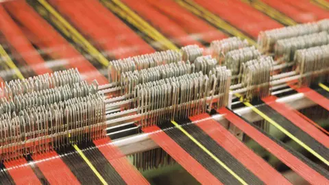 A textile loom in operation with a range of red, black and yellow threads