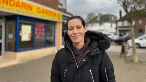 A woman with black hair in a black puffer jacket. 