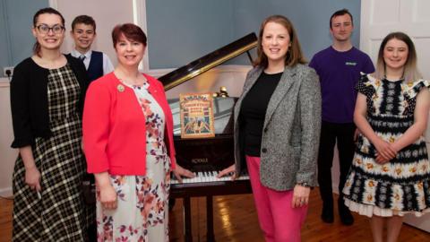 People stand next to a piano