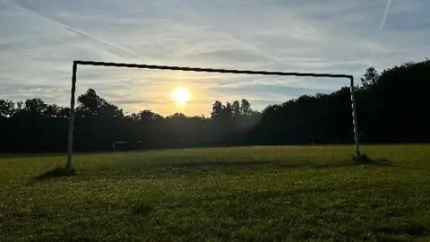 Marzy/BBC A field and a goal post with the sun coming through it 