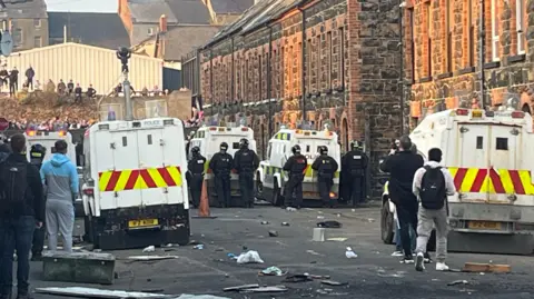 PA The back of a police line, with a number of heavily-armoured police officers beside large police vehicles. Several objects are on the ground, showing there has been signs of disorder