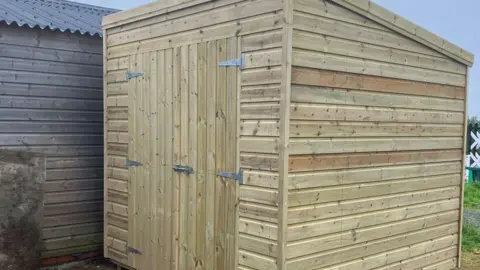 RIDING FOR THE DISABLED ISLE OF MAN A portable wooden shed with a metal bolt holding the door shut.