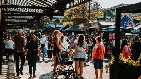 Digbeth Dining Club Crowd of people in summer clothes gathered on a waterfront queuing up to order food from street vendors