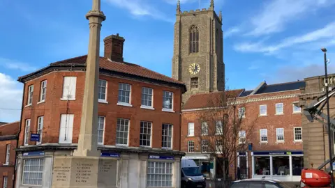 Buildings in Fakenham, with a war memorial in the foreground and a church spire in the background.