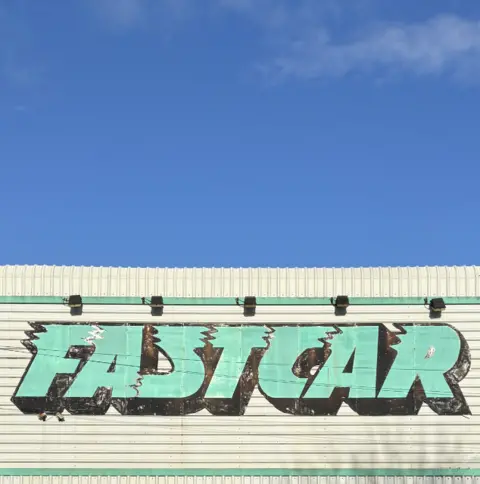 Tom Hicks A white corrugated building with a green logo painted on the side which reads: FASTCAR