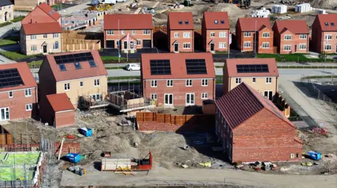 An aerial shot of a partly-built housing development, showing a range of brick-built houses, with construction sites around them.