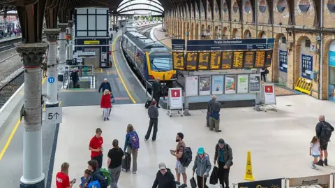Platform six at York Railway station, with a Northern train at the platform and people walking around the concourse.