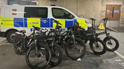 A police vehicle has a number of e-bikes propped up in front of it inside a garage