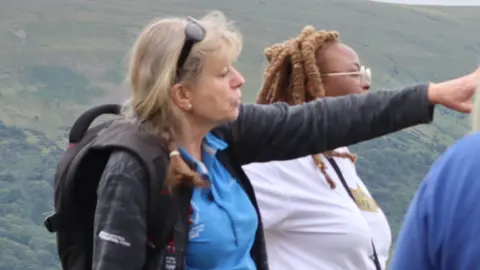 BBNP Francesca Bell wearing a team t shirt and a backpack, standing amid a crowd of colleagues in the national park with green landscape behind her