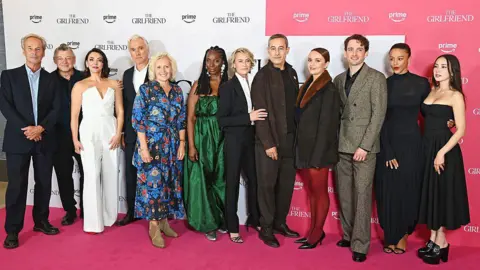 Getty Images A group of people on a red carpet all dressed up, pose for the camera.