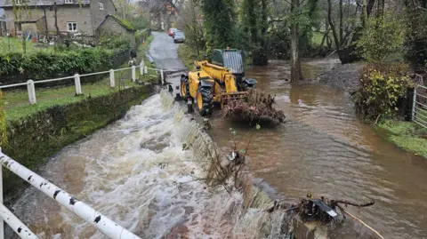 The Bridge Inn A tractor clearing debris from a flooded road. 