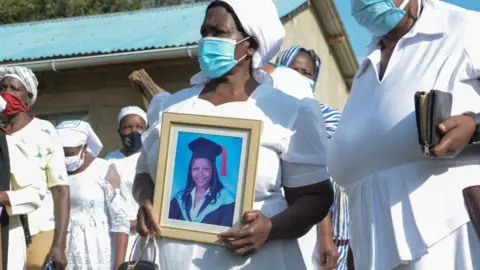 Getty Images Grace Lugaliki (2nd R) holds a portrait of her daughter Dr. Doreen Lugaliki, 39, the first Kenyan doctor who died of the COVID-19 coronavirus in Nairobi, during her daughter's funeral in Ndalu, western Kenya, on July 13, 2020