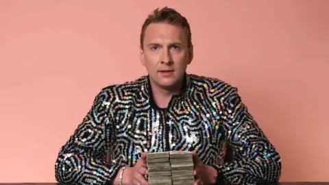 Benderslikebeckham.com Joe Lycett holds onto £10,000 in cash