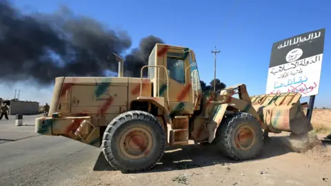 AFP A bulldozer pushes over an Islamic State group sign as Iraqi forces move towards Hawija on 4 October 2017