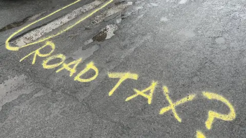 BBC/Naj Modak Graffiti next to potholes on the road