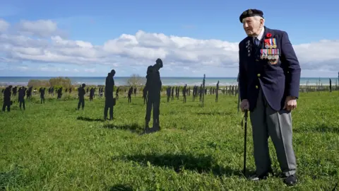 PA Media Veteran serviceman stands in front of silhouette figures