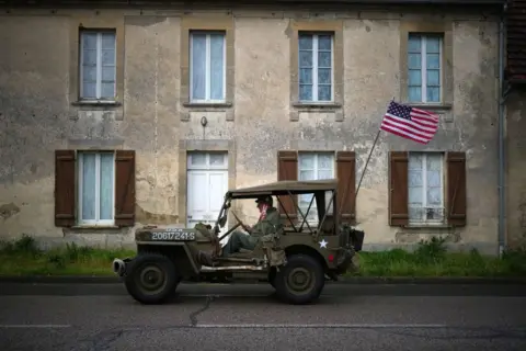  Christopher Furlong/Getty Images A man gives a victory sign as he drives a World War Two US Jeep through Colleville-sur-Mer, France