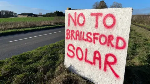 Handmade sign at side of road which reads "No to Brailsford Solar"