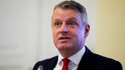 Reuters Defence Minister Luke Pollard, with short grey hair, wearing a white shirt, red tie and black suit.

