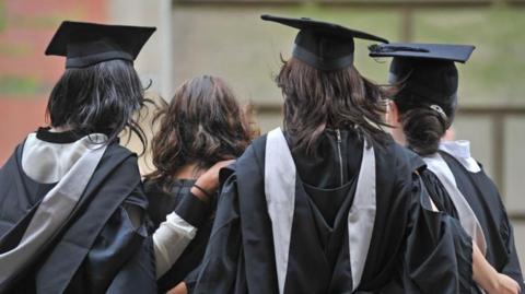 A group of female students seen from behind wearing gowns and mortar boards
